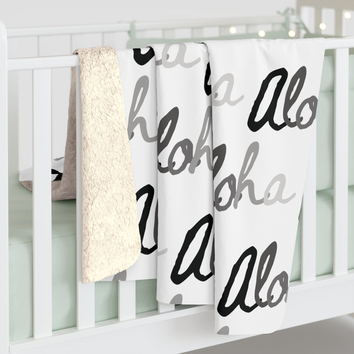 Aloha grayscale sherpa fleece blanket with a repeating black, white and gray island-inspired design draped over a white crib.