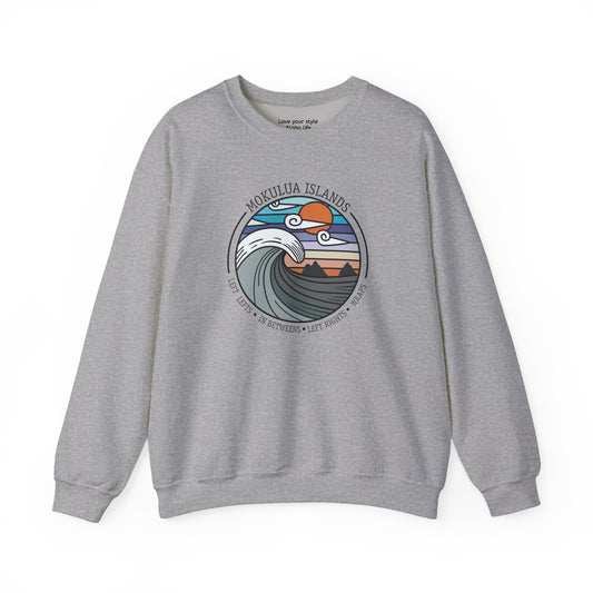 A heather gray crewneck sweatshirt featuring a circular graphic print on the chest depicting the Mokulua Islands with stylized waves, mountains, and a sun, with the text 'MOKULUA ISLANDS' and list of surfbreaks.