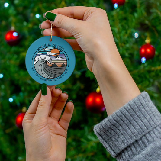 Blue ceramic ornament with Mokulua Islands surf design featuring a curling wave, sunset and Nā Mokulua off Kailua, Hawaiʻi.