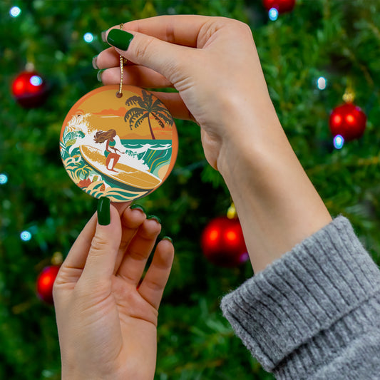 Round ceramic ornament featuring a retro Castle Point surf scene with woman surfer, tropical waves, palm tree and orange sunset.