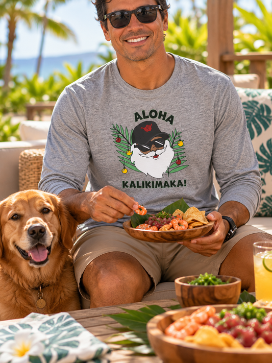 Man wearing a grey Aloha Kalikimaka long sleeve Christmas tee while enjoying a pupu plate with his dog on a tropical Hawaiʻi lanai.