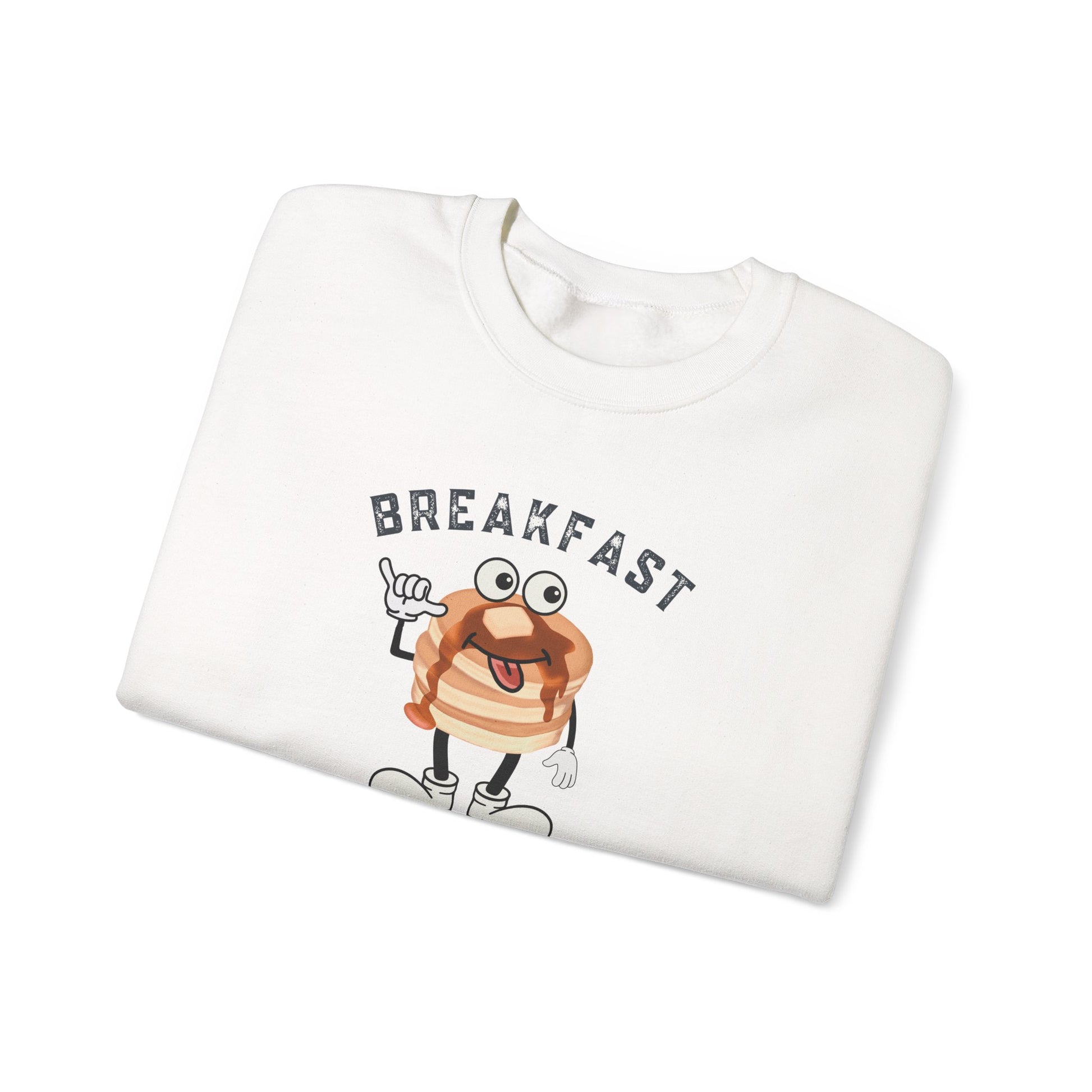 A folded white crewneck sweatshirt featuring a cartoon graphic of a pancake character with the word 'BREAKFAST' printed above it, set against a plain white background.