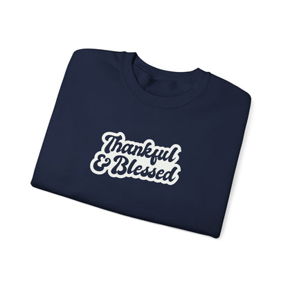A folded navy crewneck sweatshirt with 'Thankful & Blessed' printed in white script with a brown outline on the front, set against a plain white background.