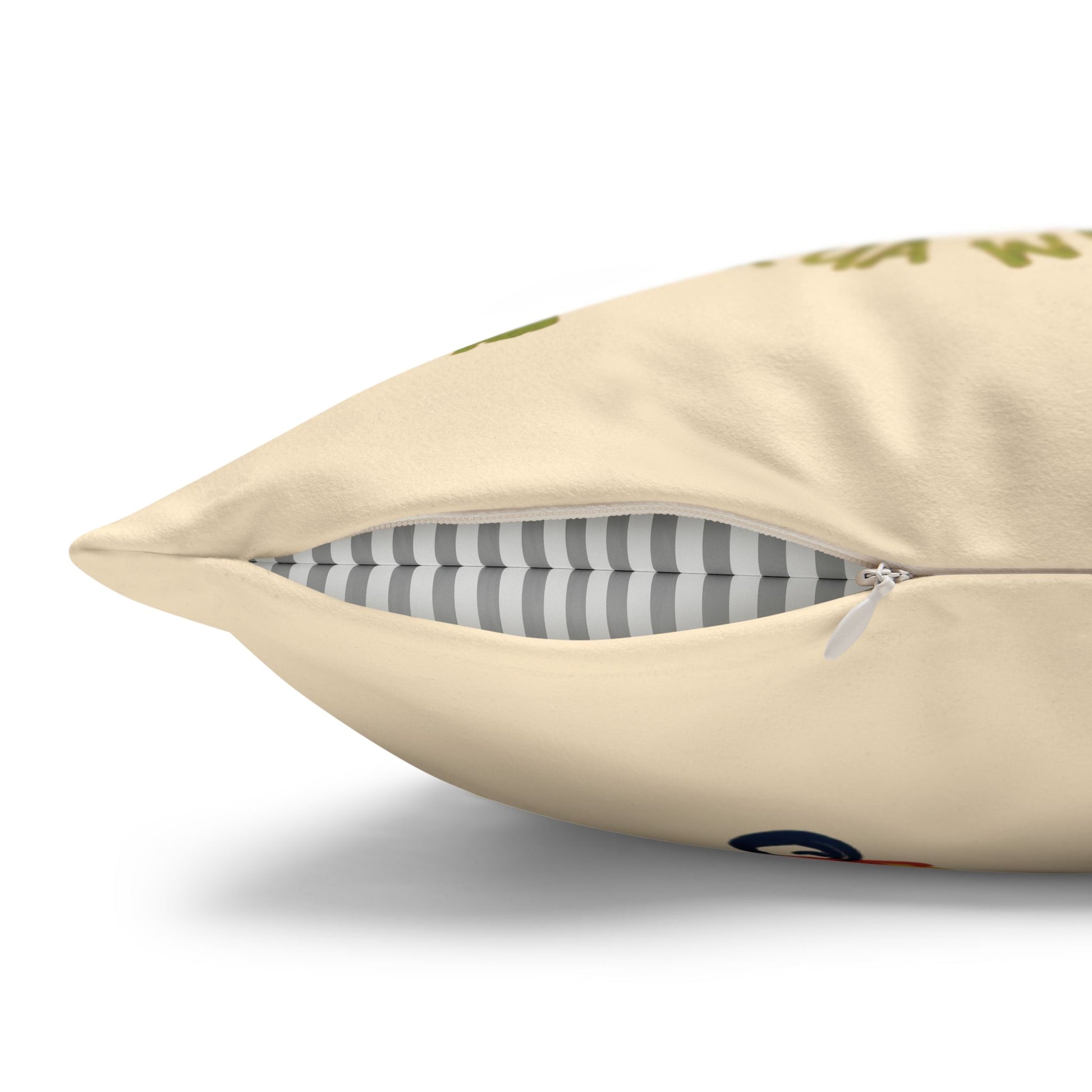 A close-up of a cream-colored throw pillow with a zipper opening, showing a gray and white striped inner cushion and a small green graphic print on the front.
