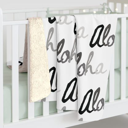 Aloha grayscale sherpa fleece blanket with a repeating black, white and gray island-inspired design draped over a white crib.