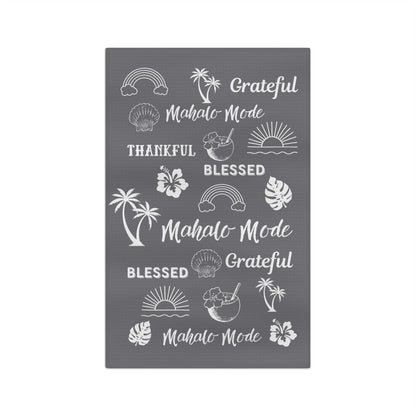 A gray micro fiber kitchen towel with white tropical-themed illustrations and phrases including rainbows, palm trees, hibiscus flowers, seashells, and the words 'Grateful,' 'Blessed,' and 'Mahalo Mode'