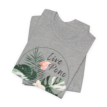 A folded heather gray t-shirt featuring a tropical graphic with green palm and monstera leaves, a pink flamingo, and the text 'Live Pono' inside a circular outline, shown on a plain white background.