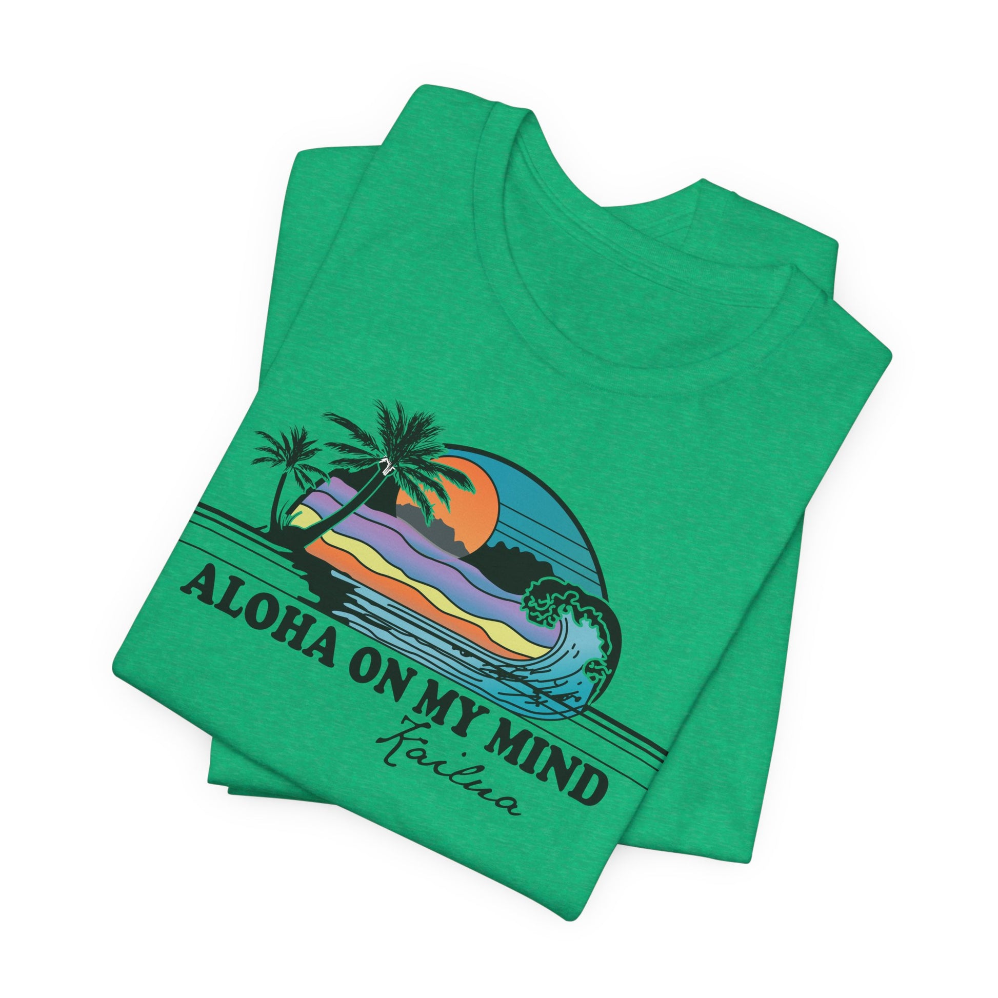 A folded green t-shirt with a colorful graphic of a Hawaiian beach scene and the text 'ALOHA ON MY MIND' and 'Kailua' printed on the front, set against a plain white background.