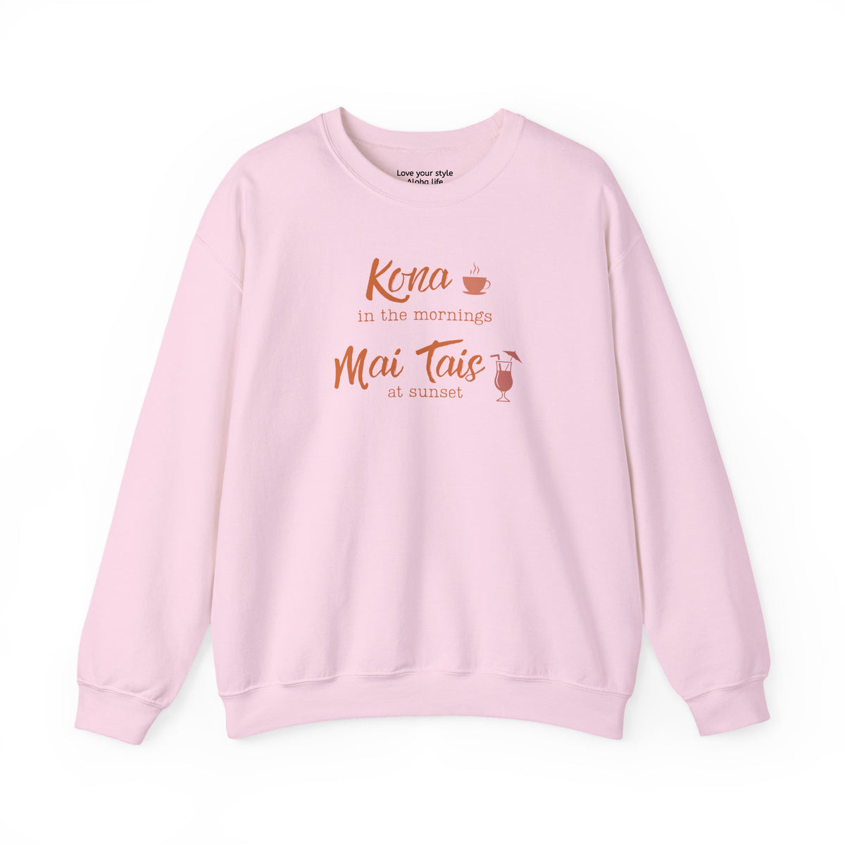 A light pink crewneck sweatshirt with a coral orange graphic print on the front that reads 'Kona in the mornings Mai Tais at sunset' with a small coffee cup and cocktail glass illustration.