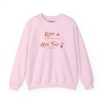 A light pink crewneck sweatshirt with a coral orange graphic print on the front that reads 'Kona in the mornings Mai Tais at sunset' with a small coffee cup and cocktail glass illustration.