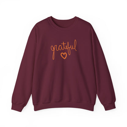 A maroon crewneck sweatshirt featuring the word 'grateful' in orange cursive script and a matching orange heart outline on the chest, displayed against a solid white background.