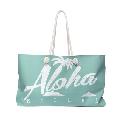 A mint green tote bag with white rope handles, featuring a white graphic print of the word 'Aloha' in script over a palm tree and islands, with 'KAILUA' printed below in block letters. The bag is shown against a plain white background.