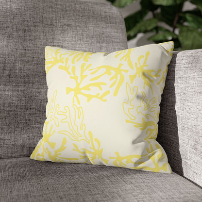 A square throw pillow with a yellow abstract coral pattern on an off-white background, resting on a textured gray fabric armchair.