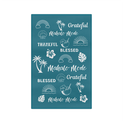 A rectangular teal kitchen towel featuring white tropical-themed illustrations and phrases including rainbows, palm trees, hibiscus flowers, seashells, sunsets, and repeated text reading 'Grateful Mahalo Mode' and 'Blessed Mahalo Mode' on a white background.