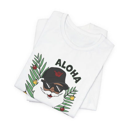 Folded white Santa Kalikimaka unisex T-shirt with hand-drawn Santa wearing sunglasses and throwing a shaka surrounded by tropical palm leaves.