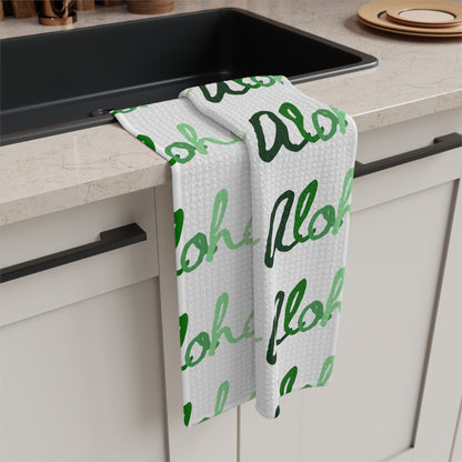 Green Aloha Hawaiʻi kitchen towel with repeating script design in light and dark green on white draped over kitchen sink