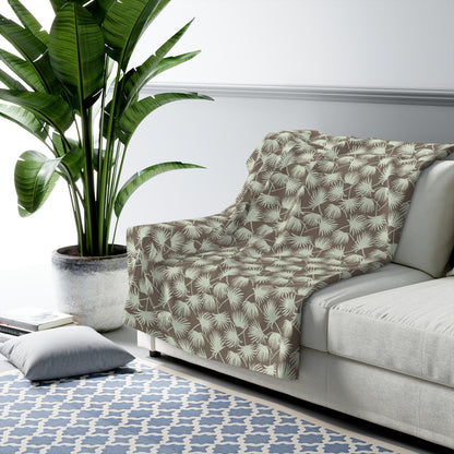 Fan Palm Mocha Mint sherpa fleece blanket with a repeating mint palm leaf pattern on a warm mocha background draped on a grey couch.
