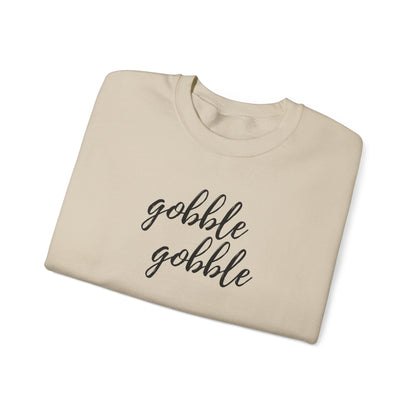 A folded beige crewneck sweatshirt with the phrase 'gobble gobble' printed in black cursive script across the chest, shown on a clean white background.