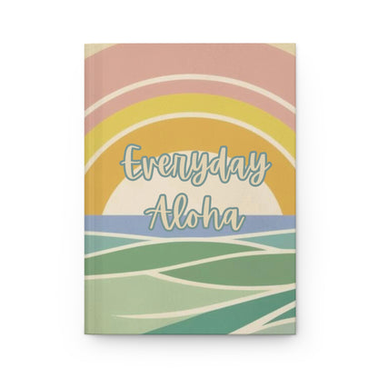 A hardcover notebook with a retro sunset and ocean design, featuring the text 'Everyday Aloha' in light blue script. The cover has pastel stripes and waves in pink, yellow, blue, green, and cream, set against a plain white background.