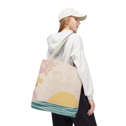 A woman wearing a white cap and white hoodie carries a canvas tote bag with a pastel sunset and palm tree design, shown from a three-quarters back view against a plain white background.