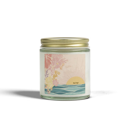 A glass jar candle with a gold metal lid and a pastel tropical sunset label, shown on a clean white background with a soft shadow.