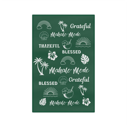 A dark green kitchen towel with white tropical-themed illustrations and repeated phrases including 'Grateful Mahalo Mode,' 'THANKFUL,' 'BLESSED,' and 'Mahalo Mode.'.