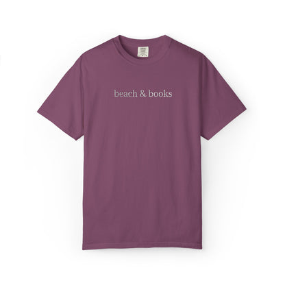 A purple comfort colors tee with 'beach & books' embroidered in white.