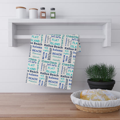 A white kitchen towel with a blue and aqua 'Kailua Surf Breaks' text pattern hanging in a kitchen setting
