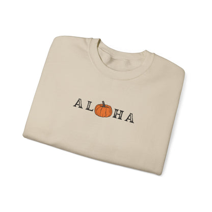 A folded beige crewneck sweatshirt featuring a graphic print of the word 'ALOHA' with the letter 'O' replaced by an orange pumpkin illustration, set against a plain white background.