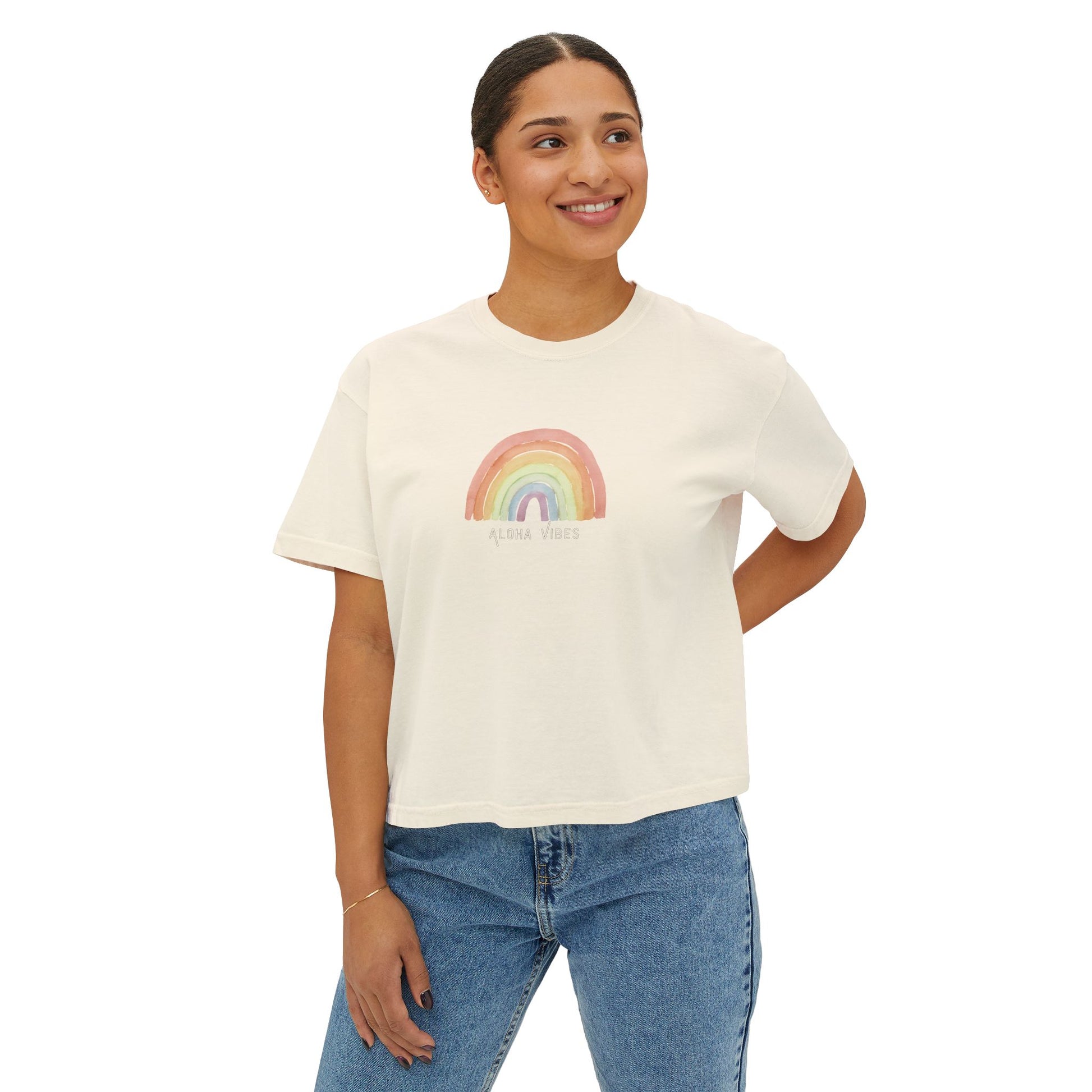 A woman wearing an off white short-sleeve crop top t-shirt featuring a colorful watercolor-style rainbow graphic on the chest with the text 'ALOHA VIBES' underneath, displayed on a clean white background.