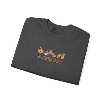 A folded dark grey crewneck sweatshirt featuring a central graphic of a dog under a blanket, house slippers, coffee cups and the word 'HOMEBODY' printed below it.