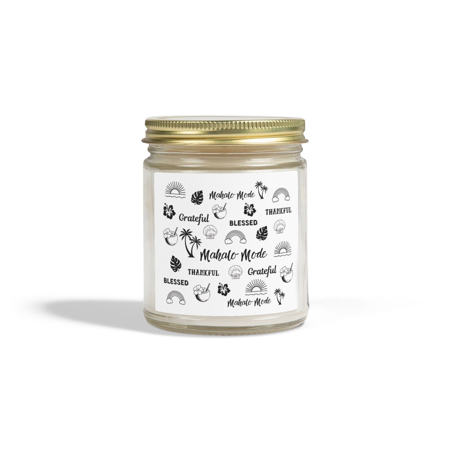 A glass jar candle with a gold metal lid and a white paper label featuring black tropical-themed illustrations and text like 'Mahalo Mode,' 'Grateful,' and 'Blessed,' shown on a clean white background.