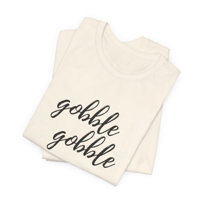 A folded cream-colored t-shirt with the phrase 'gobble gobble' printed in black cursive script across the front, displayed on a clean white background.