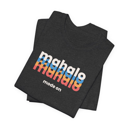 A folded dark heather gray t-shirt with a retro-style graphic reading 'mahalo mahalo' in white, blue, orange, and red gradient letters, with 'mode on' printed below in white, on a clean white background.