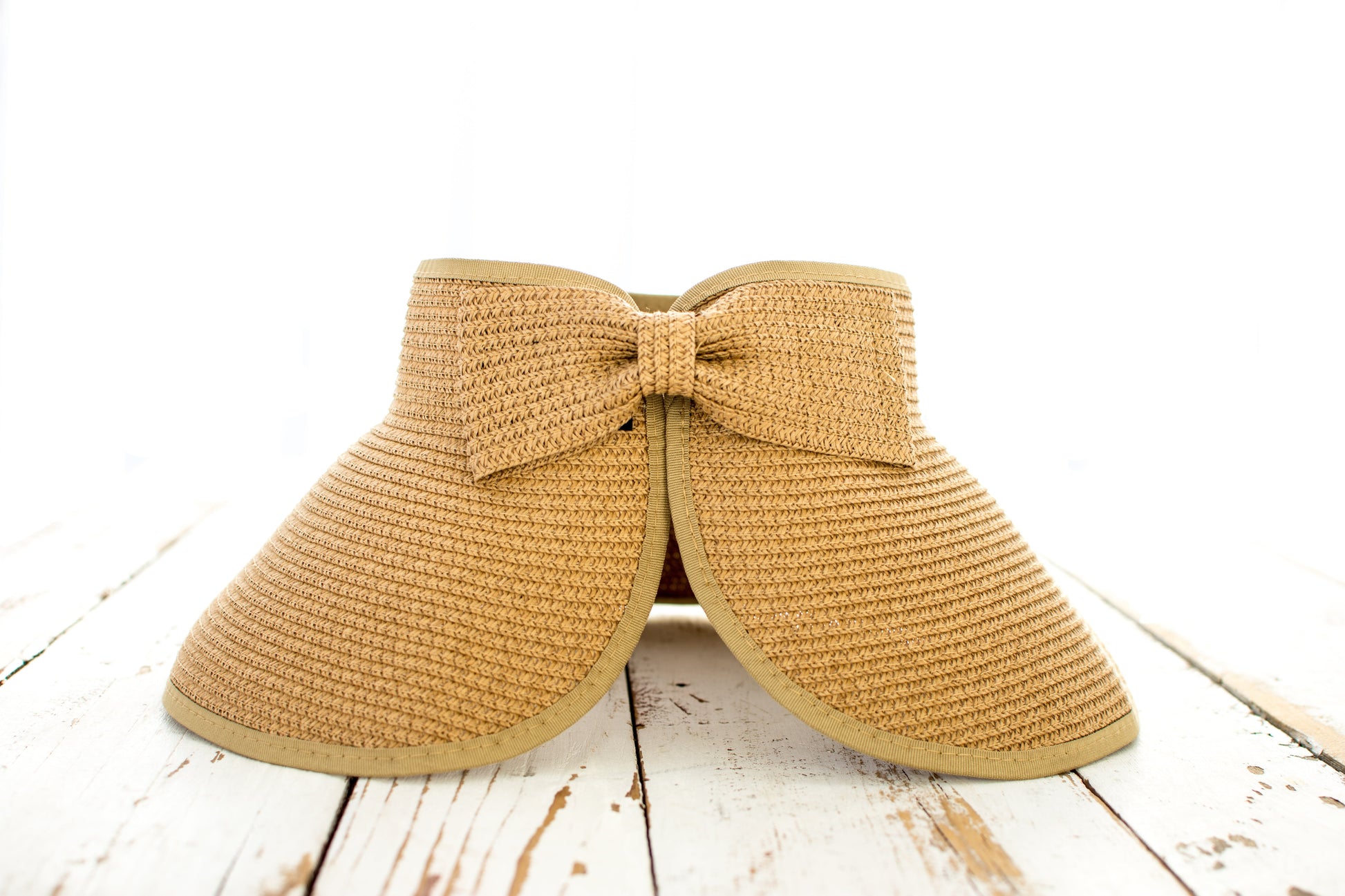 Beige straw visor hat with a bow on a wooden surface