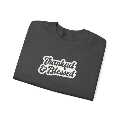 A folded dark grey crewneck sweatshirt with 'Thankful & Blessed' printed in white script with a brown outline on the front, set against a plain white background.