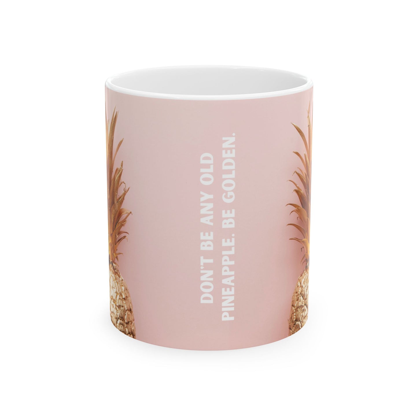 A light pink ceramic mug featuring a vertical white text print that reads 'DON'T BE ANY OLD PINEAPPLE, BE GOLDEN.' flanked by illustrations of golden pineapples on the sides.