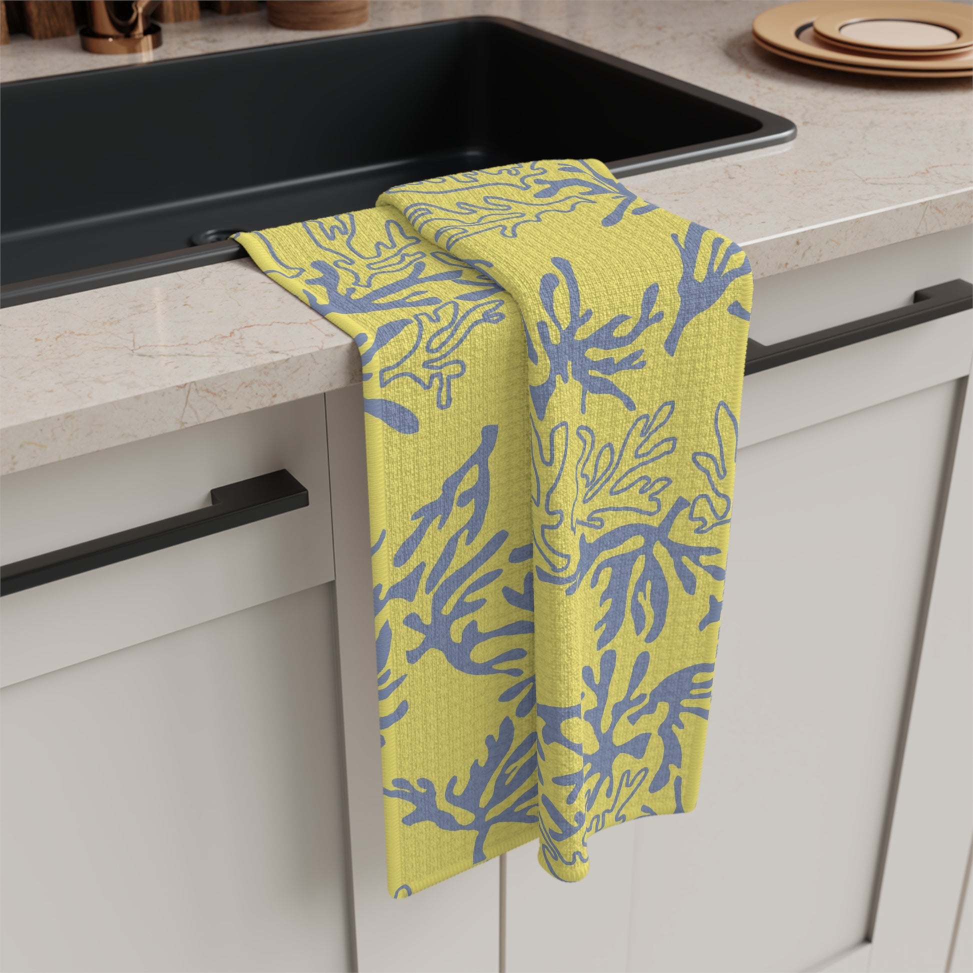 Coral Yellow and Grey microfiber kitchen towel featuring an original island-inspired coral reef pattern by Global Village Kailua draped over the edge of a black sink in a modern kitchen setting.