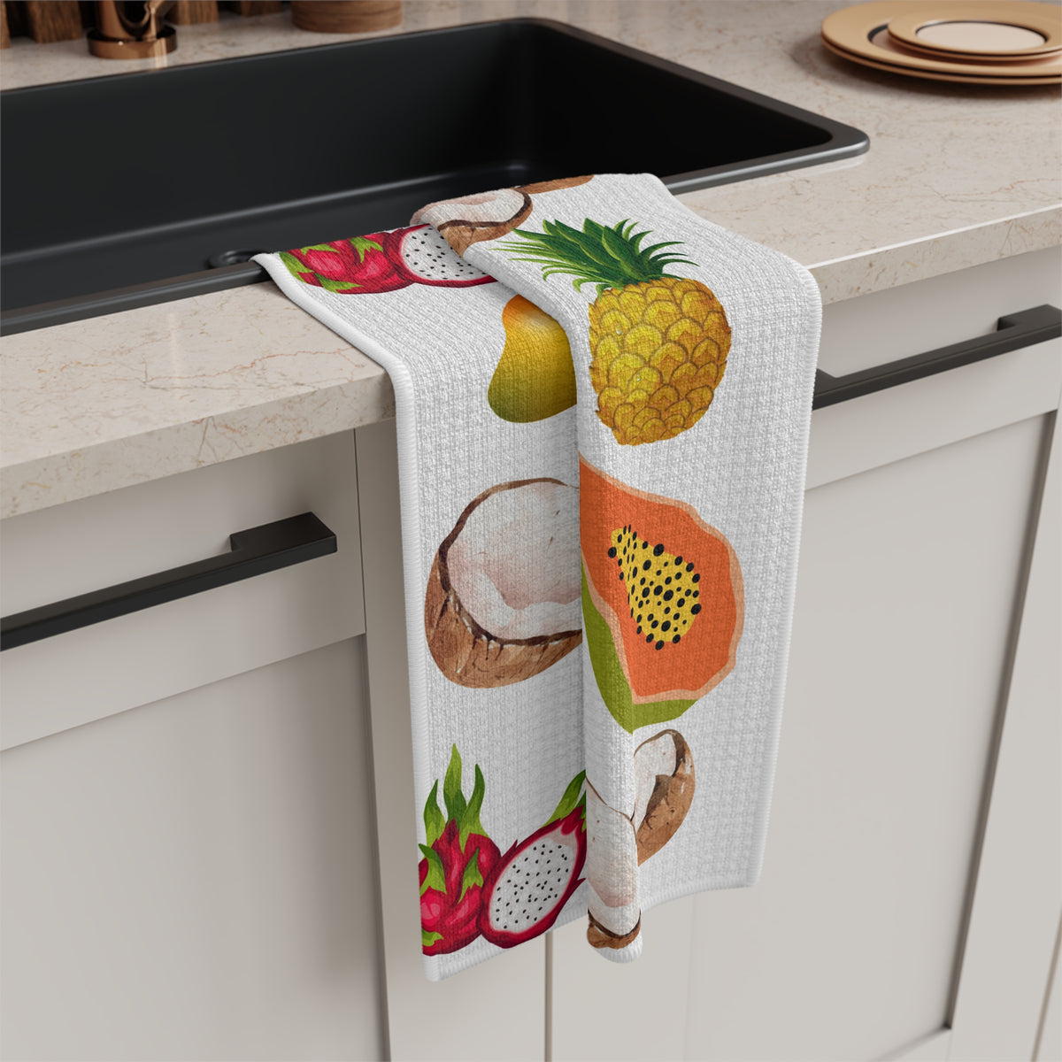 A white kitchen towel with a colorful tropical fruit print, draped over the edge of a black sink in a modern kitchen setting.