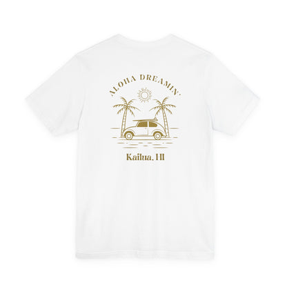 A white short-sleeve t-shirt shown from the back, featuring a gold-colored retro graphic of a classic car between two palm trees with the text 'ALOHA DREAMIN'' and 'Kailua, HI'.