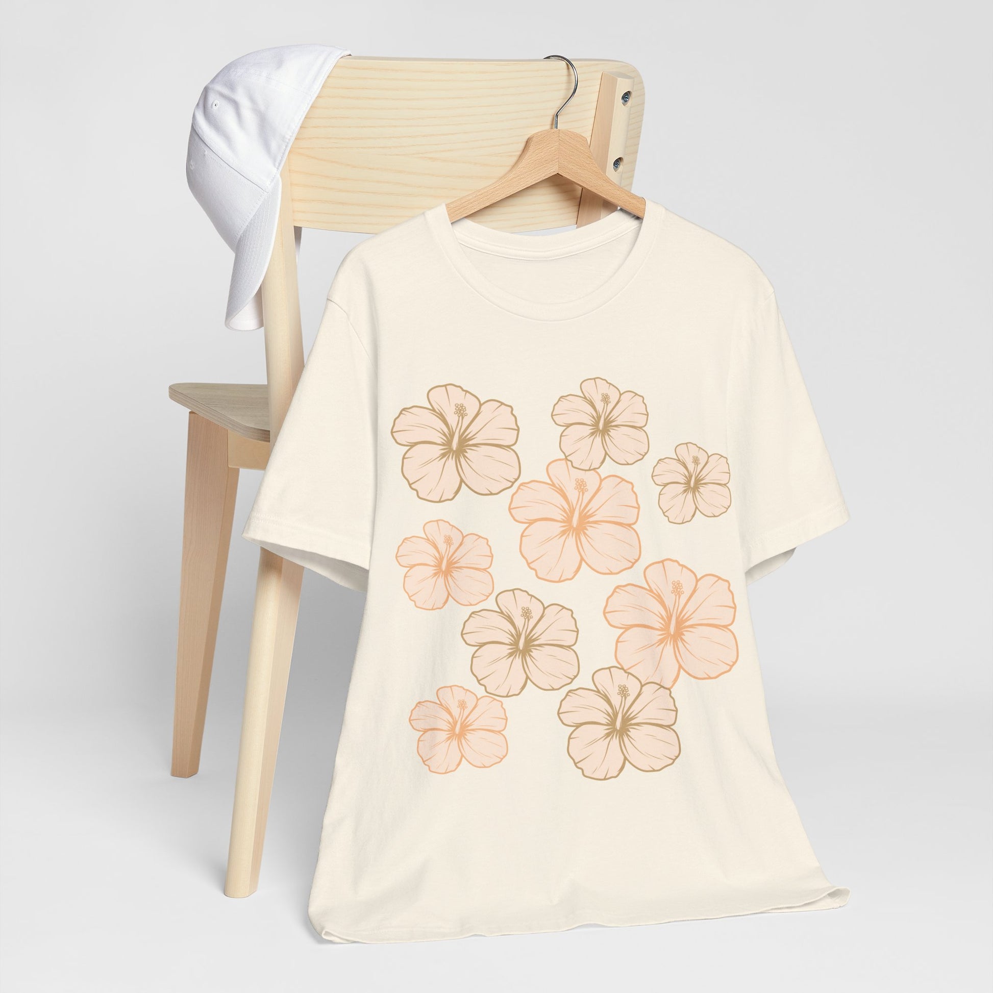 Off White Hibiscus All Over Graphic Tee featuring scattered tropical hibiscus flowers on a soft unisex tee inspired by island life in Hawaii hanging on a wood chair.