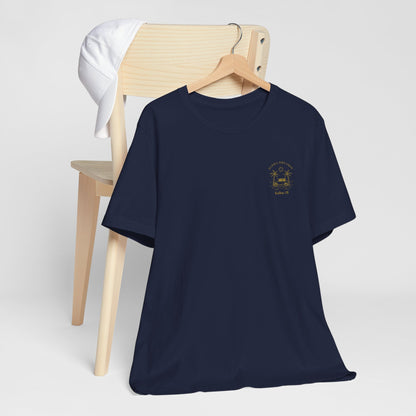 A navy crewneck t-shirt with a small gold 'Aloha Dreamin Kailua Hawaii' design on the left chest, displayed on a wooden hanger draped over a light wood chair with a white shirt hanging off the backrest, against a neutral light gray background.