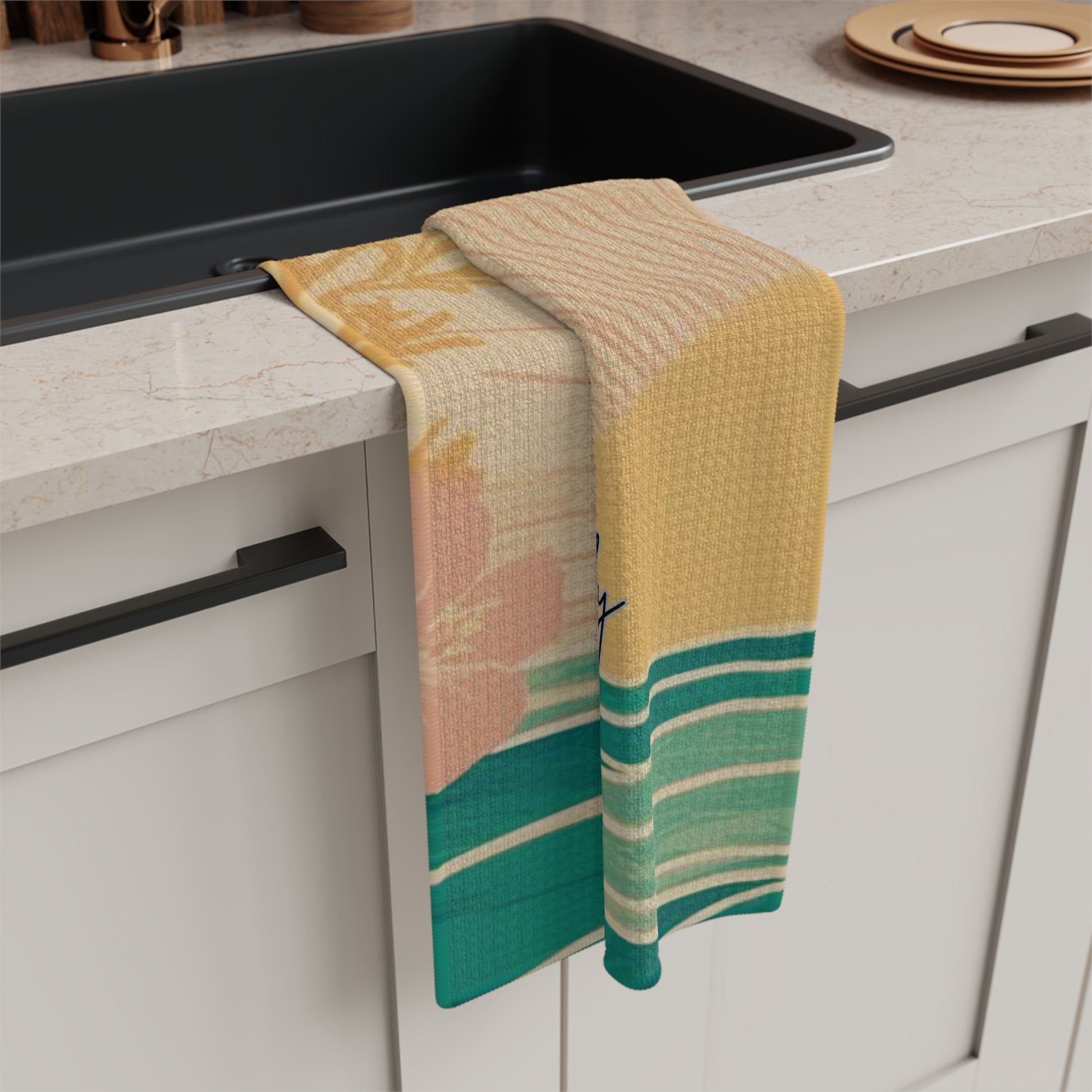 A kitchen towel with a tropical floral print hangs over the edge of a black sink in a modern kitchen. The towel features a textured waffle pattern and a color palette of yellow, peach, pink, and green.