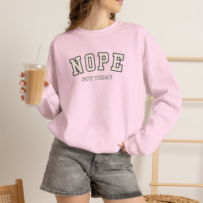 A woman wearing a light pink crewneck sweatshirt with the text 'NOPE NOT TODAY' printed on the front in black and white, paired with gray denim shorts and holding an iced coffee.