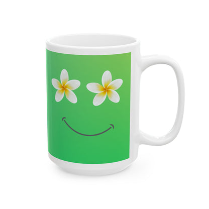 A white ceramic mug featuring a green background on the front with two white plumeria flowers acting as eyes and a simple black smiley curve below, shown on a plain white background.