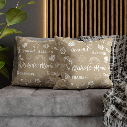 Two beige throw pillows with white tropical-themed printed text and icons, styled on a gray sofa with a plaid throw blanket and a wooden slat wall background.