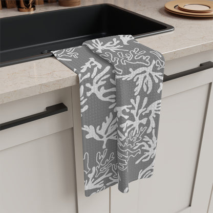 A gray kitchen towel with a white coral pattern hanging over the edge of a black sink in a kitchen setting.