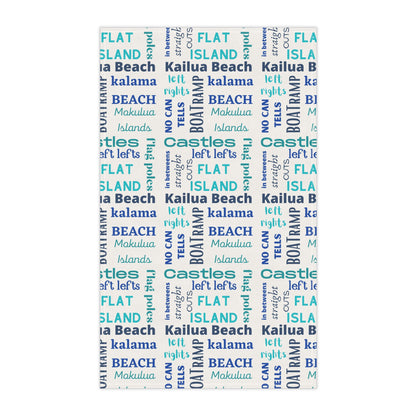 A tea towel featuring a repeating pattern of words like 'FLAT ISLAND', 'CASTLES', 'KALAMA BEACH', 'Kailua Beach', 'BOAT RAMP', and 'MOKOLUA ISLANDS' in blue, teal, and navy on a white background.
