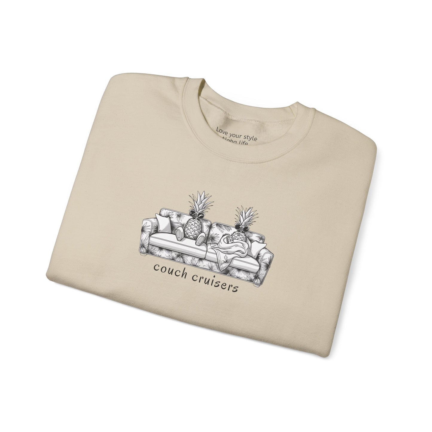 A sand-colored crewneck sweatshirt with a black and white graphic of a couch with pineapples and the text 'couch cruisers', folded with white background.