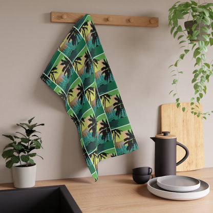 A kitchen towel with a green and black palm tree pattern 'Kailua Hawaii' hanging on a wooden peg rack on a beige wall above a wooden countertop with kitchen items.